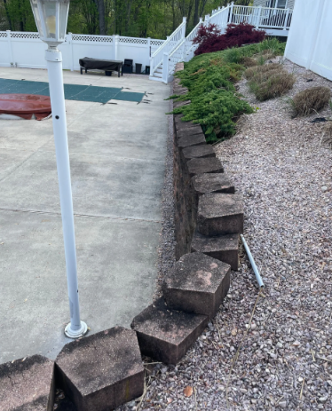 Concrete retaining wall with landscaping and a pool area.