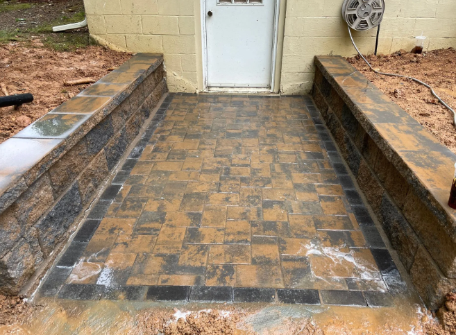 Stone-paved walkway and raised walls lead to a white door. The ground is wet with water.