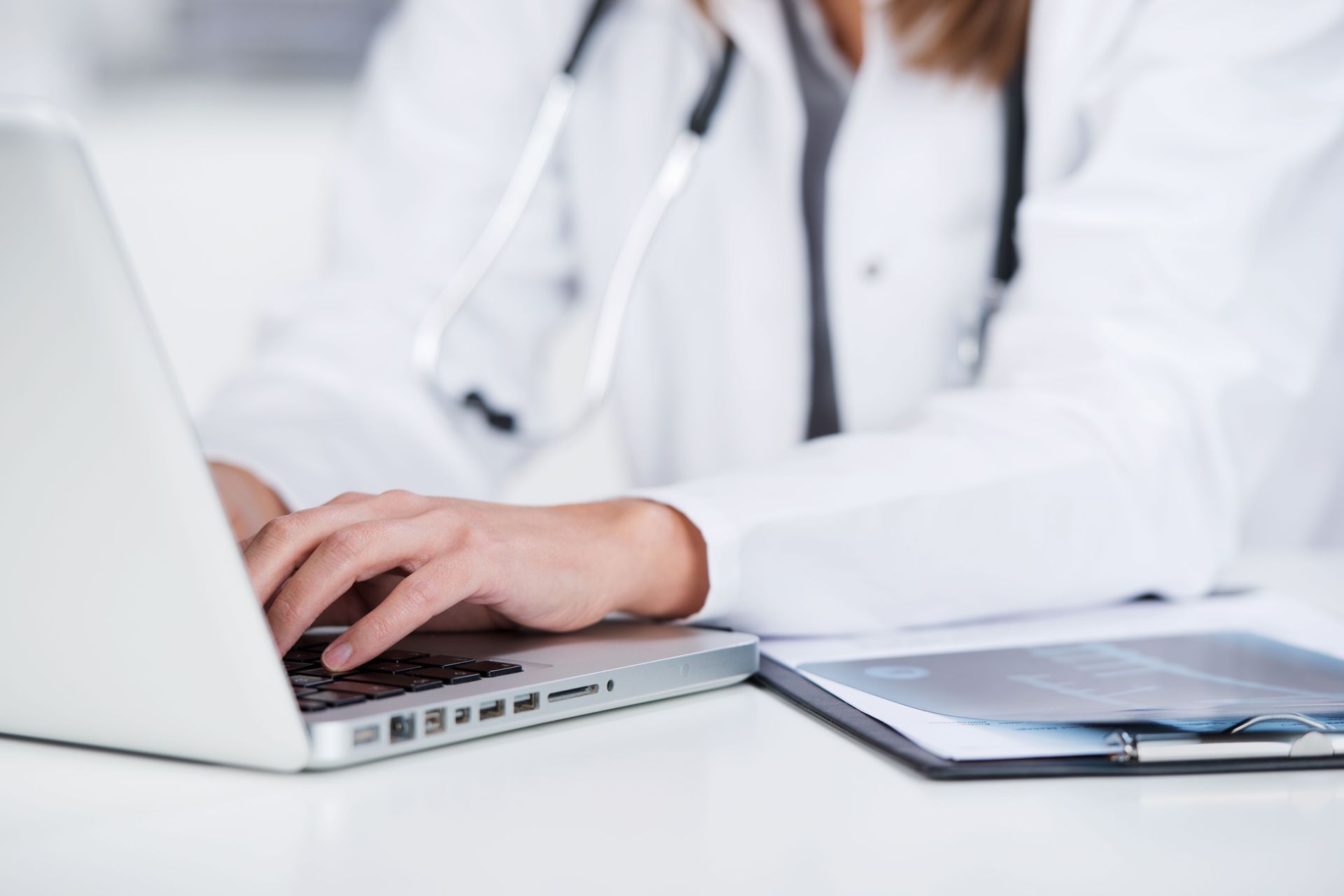 A doctor is typing on a laptop computer.