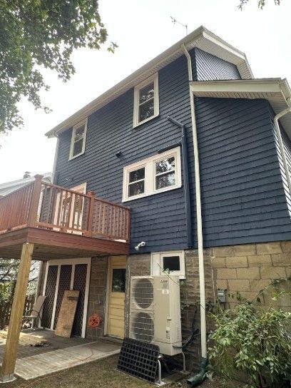 Two-story house with dark blue siding, deck, and an HVAC unit outside.