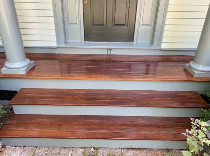 Wooden porch steps with a shiny, dark wood finish and gray trim leading to a gray door.