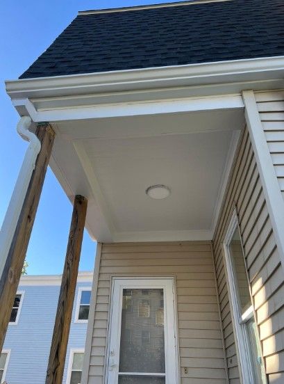 Covered porch with white ceiling, tan siding, and wooden support beams.