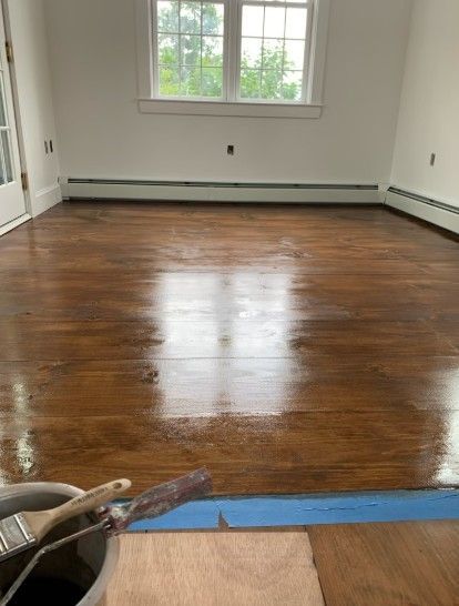 Newly finished hardwood floor in room with window and white walls. Paint supplies are visible in foreground.