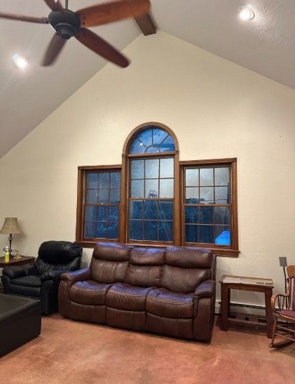 Living room with brown leather sofa, windows, and ceiling fan.