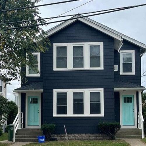 Two-story duplex with dark blue siding, white trim, and turquoise doors.