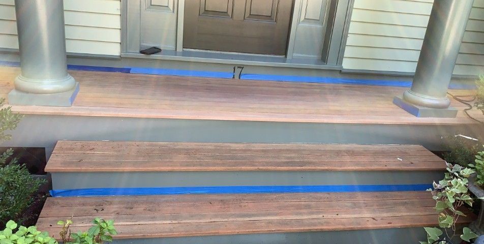 Wooden porch steps with blue painter's tape, leading to a door between two columns.