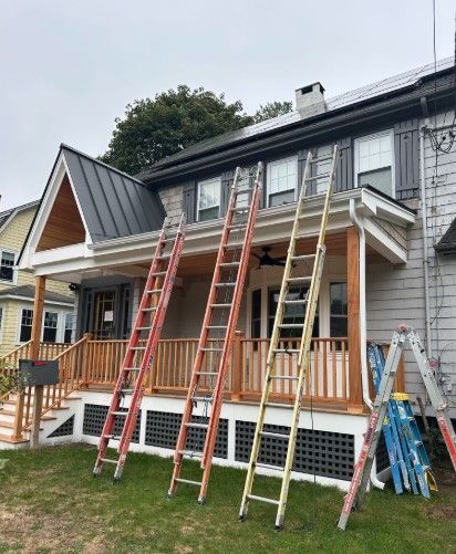 Three ladders leaning against a house with a porch; one red, one orange, one yellow.