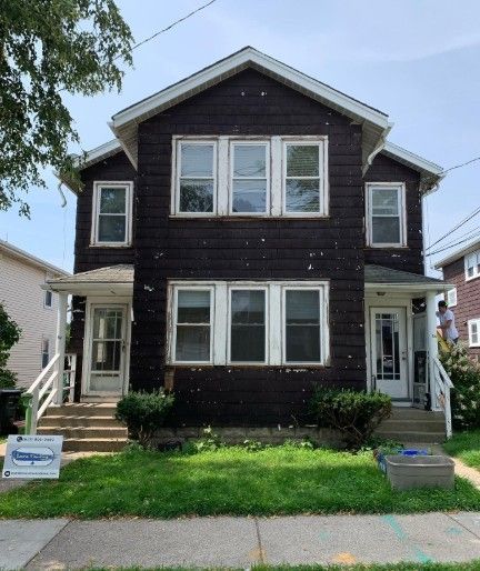 Two-story duplex with dark brown siding and white trim. Front yards with green grass and shrubbery.