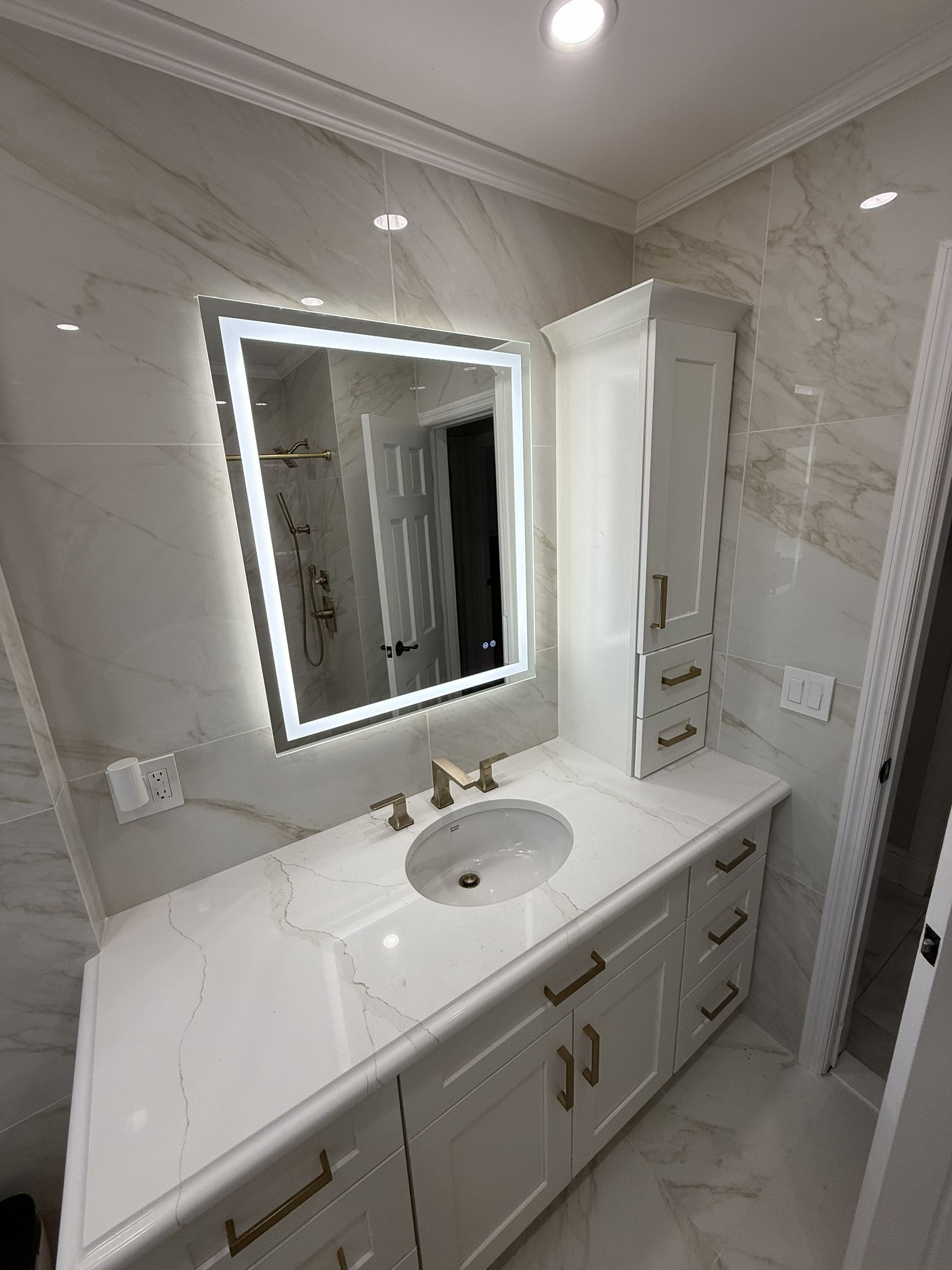 Modern bathroom vanity with lit mirror, white countertop, sink, and marble-patterned walls