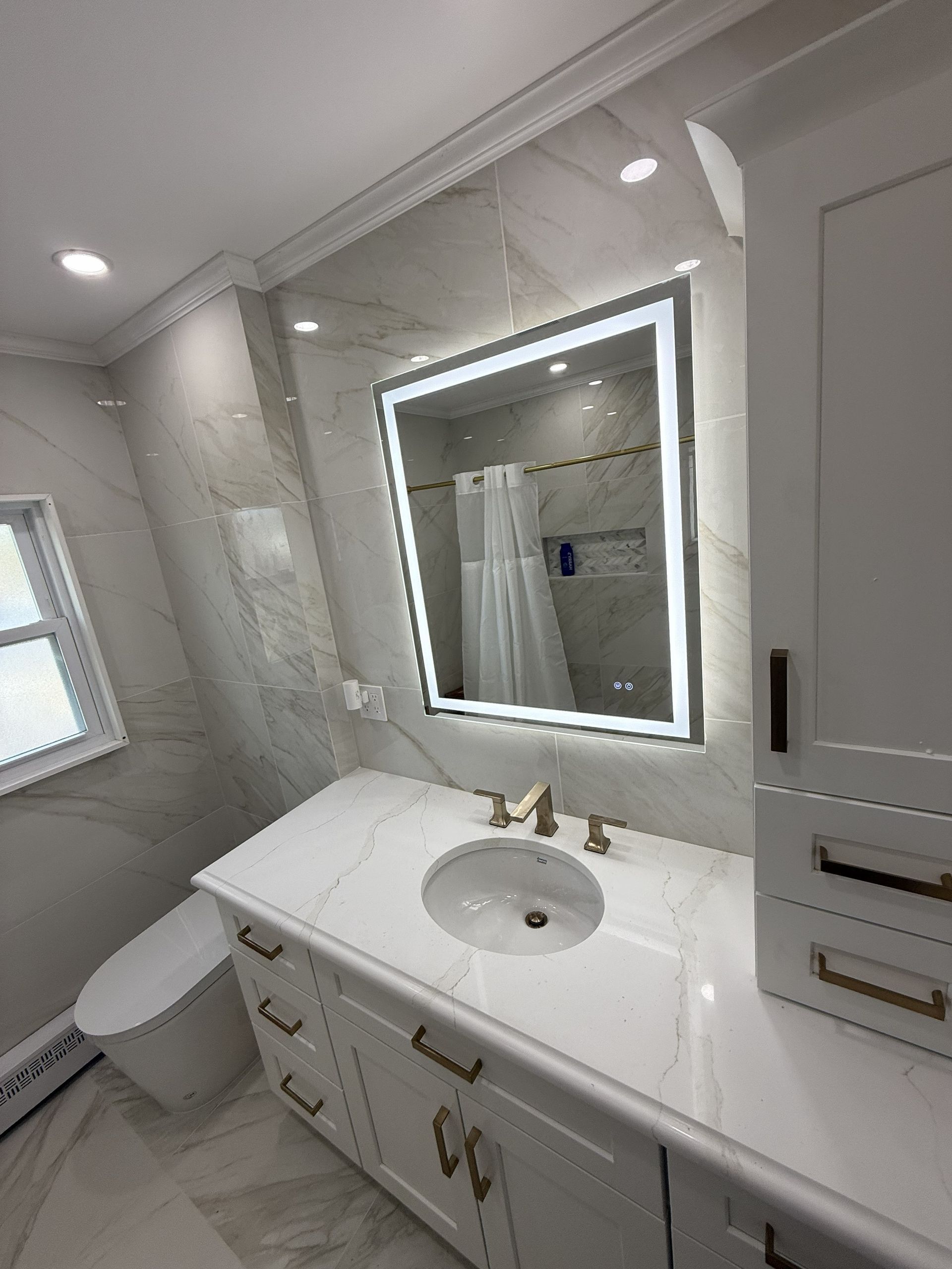 Bright white bathroom vanity with lit mirror, sink, toilet, and tiled walls