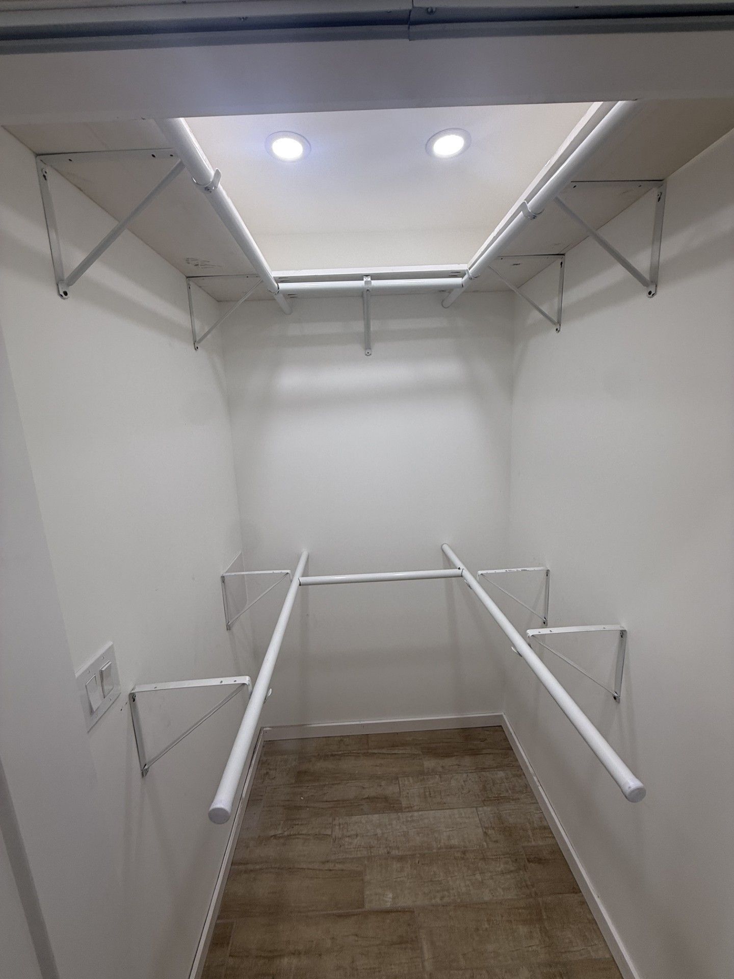 Small walk-in closet with white walls, shelves, and hanging rods, viewed from the doorway.