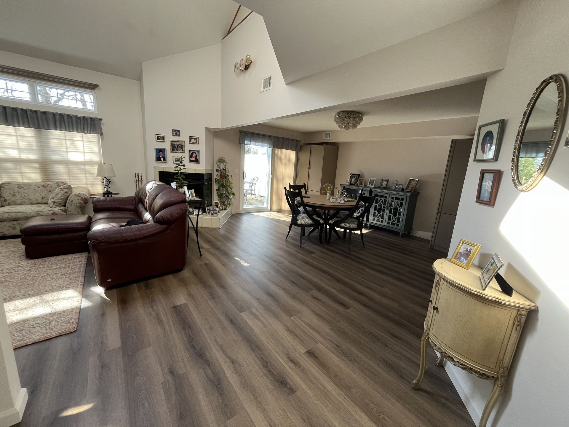 Bright open living room with brown leather sofa, dining table, wood floors, and sunlight through windows