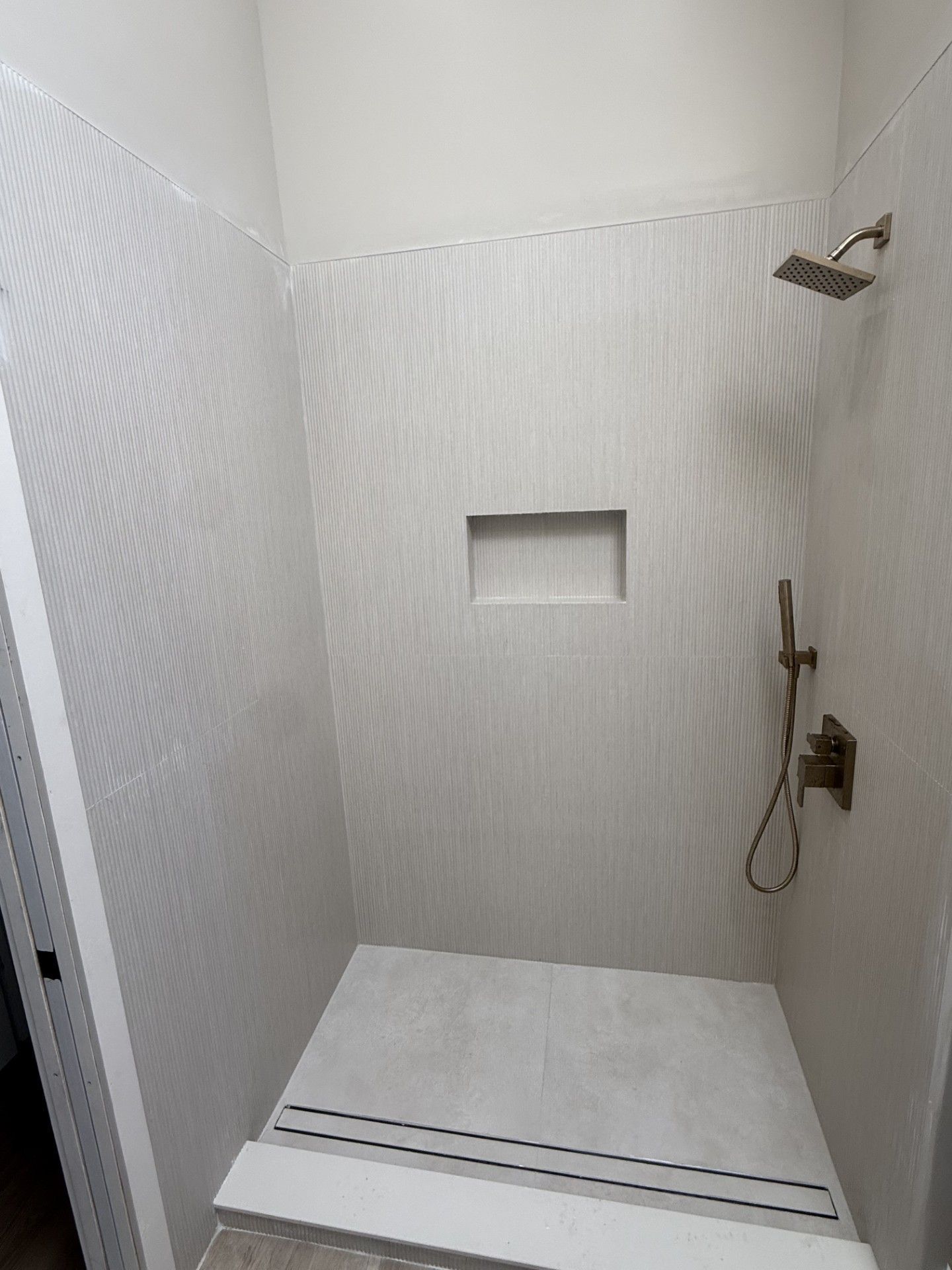 White tiled shower stall with built-in niche, bench seat, and wall-mounted shower head and controls.
