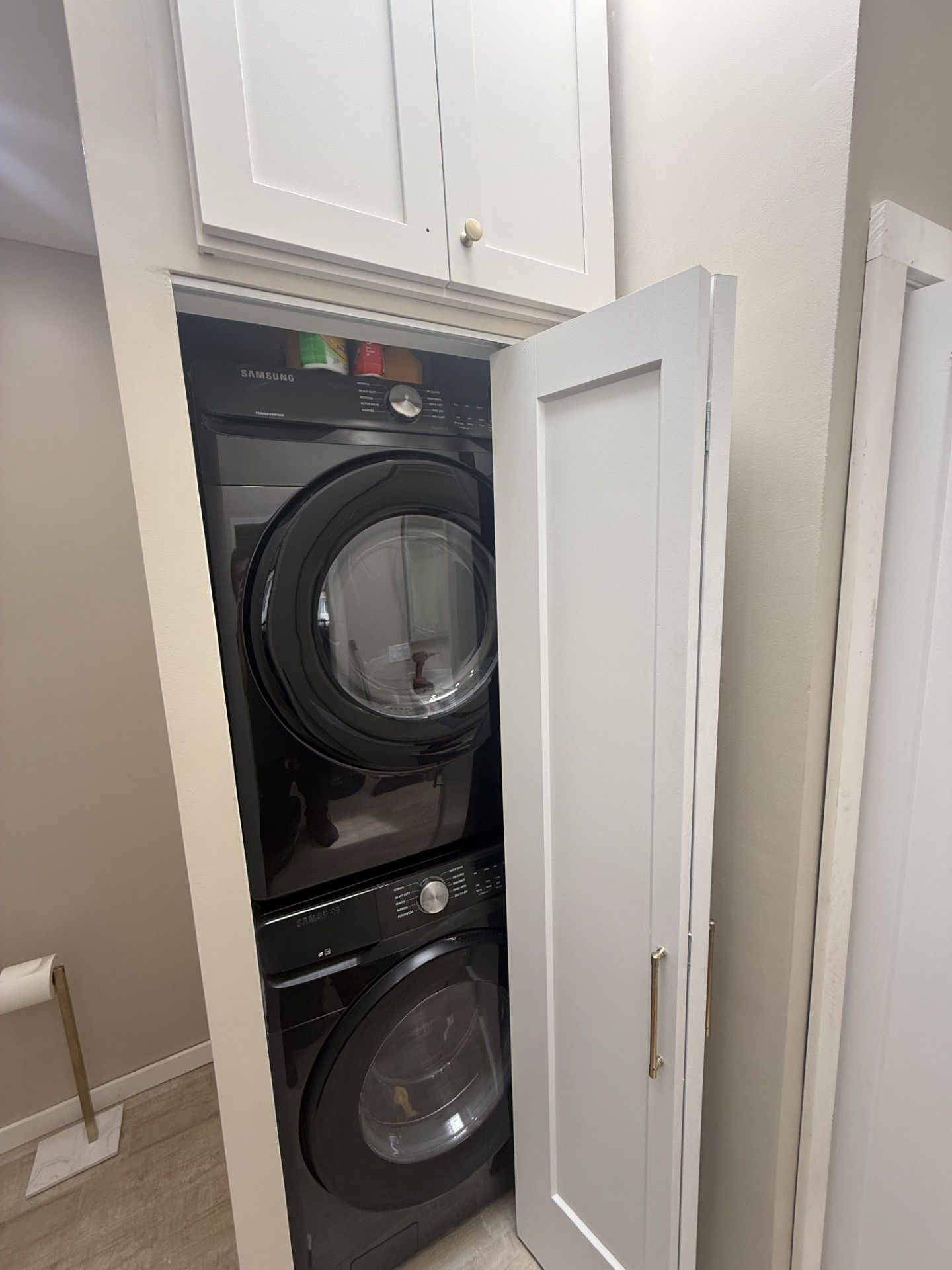 Stacked washer and dryer in a narrow laundry closet with the door open.