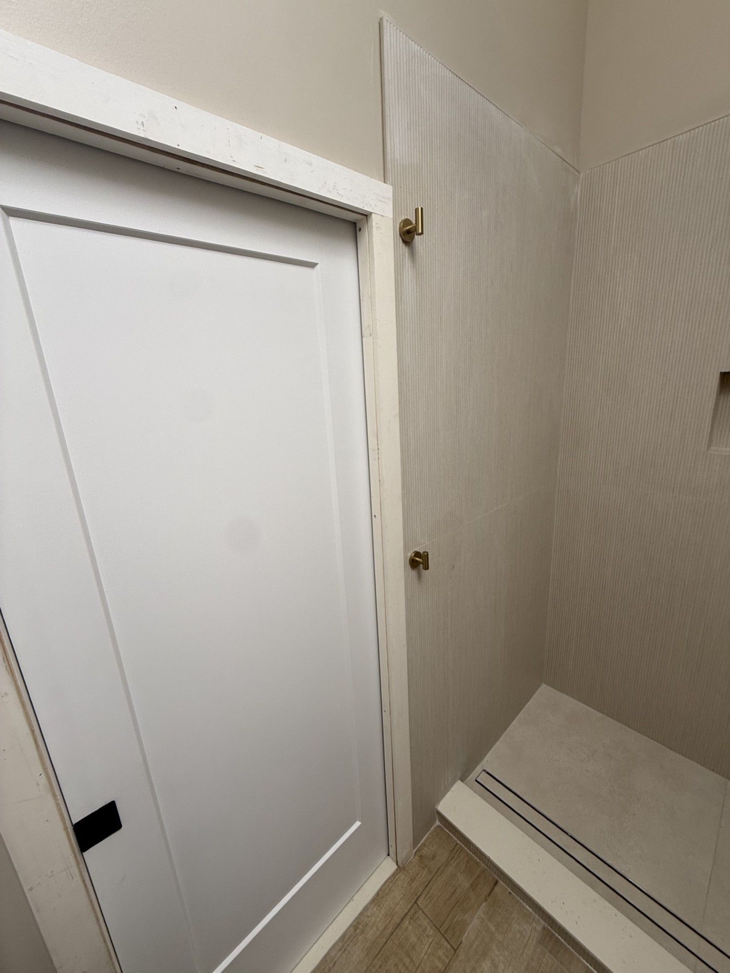 White closet door in a narrow hallway beside a partially open door and stacked white panels.