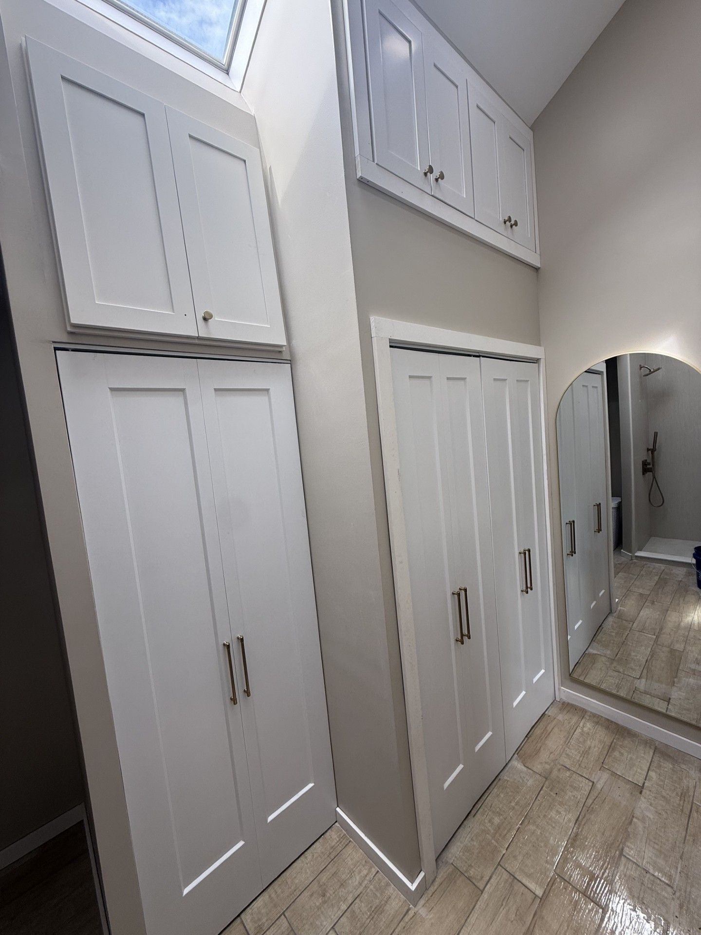 White laundry cabinets and a mirrored closet in a narrow hallway with tiled floor.