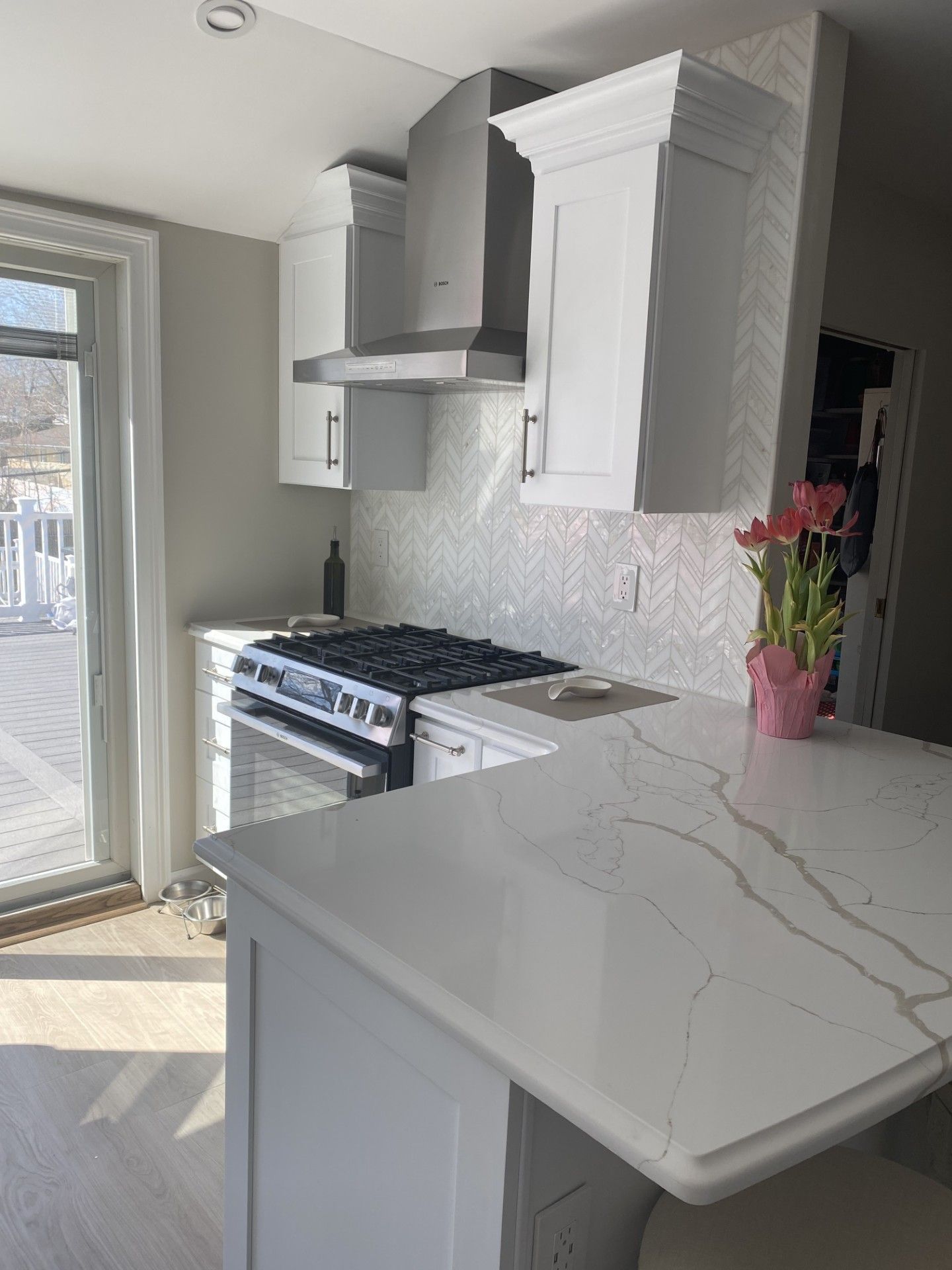 A kitchen with white cabinets, a stainless steel range hood, marble-patterned countertops, and a bouquet of tulips.