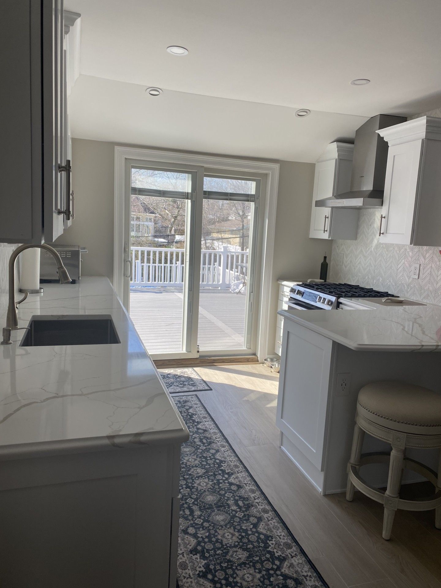 A bright, modern kitchen with white cabinets, a marble-patterned island, a sink, and a sliding door leading to a deck.