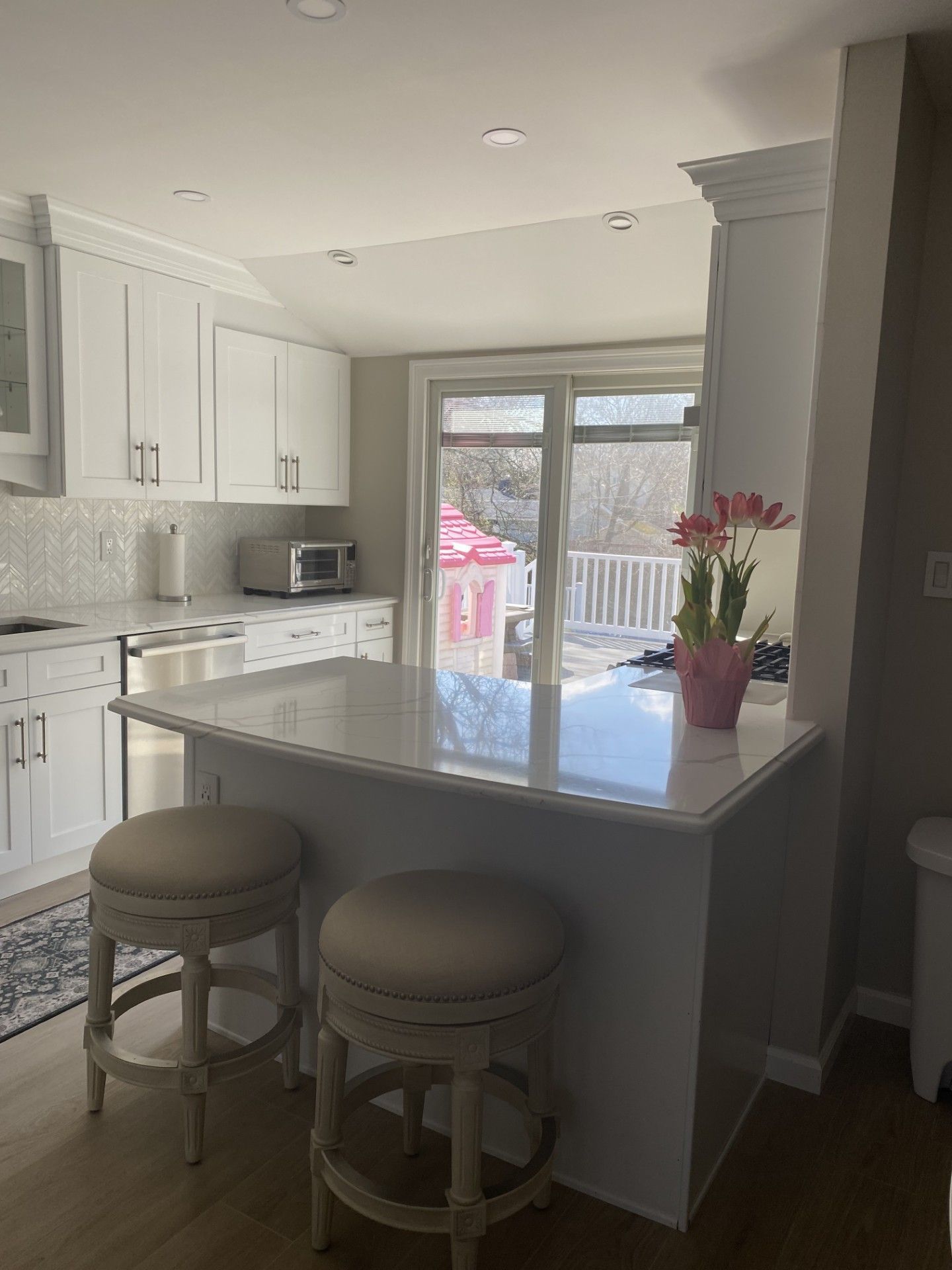 A bright kitchen featuring white cabinets, a central island with two light-colored stools, and a glass door to a deck.