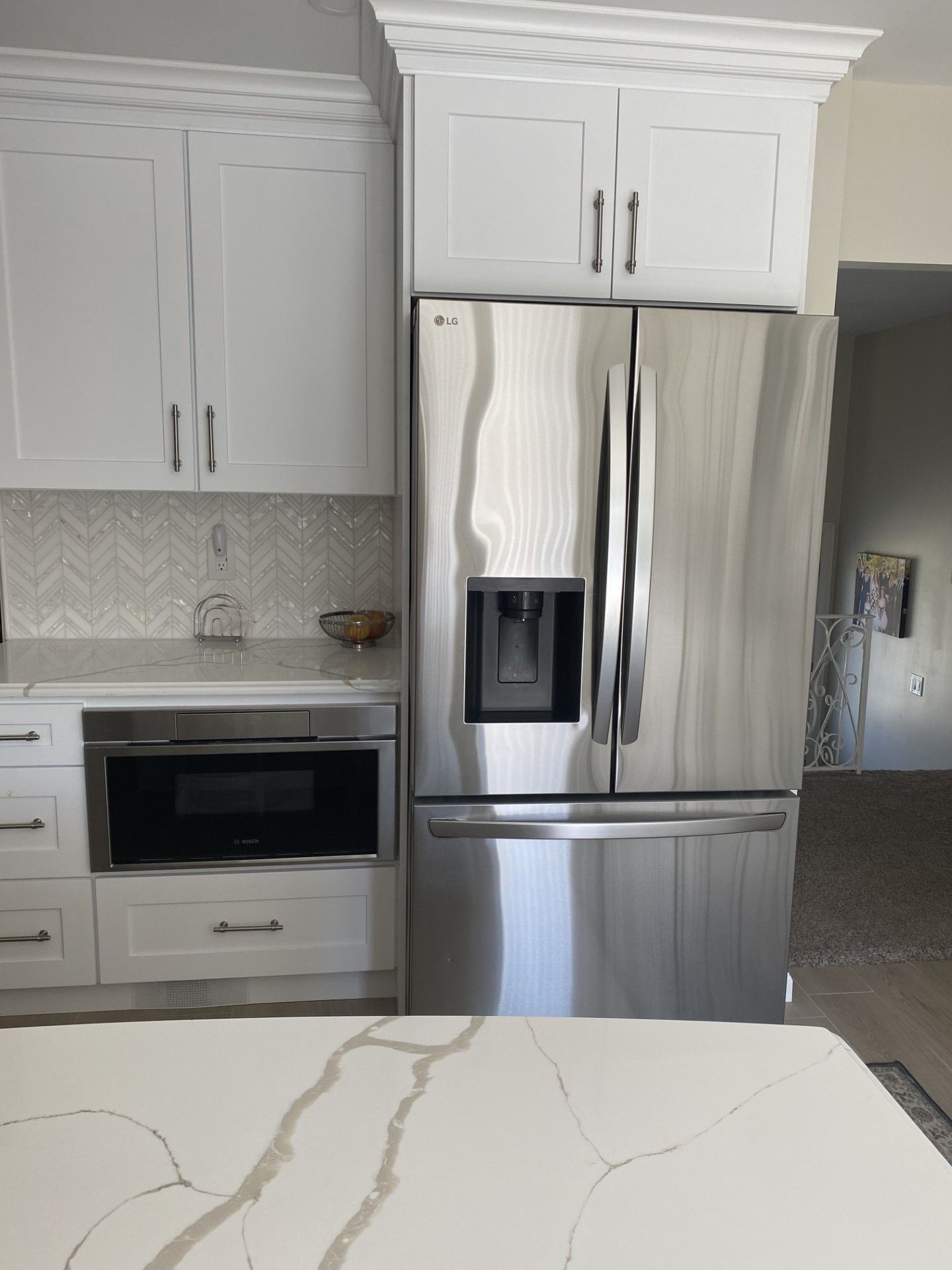 A stainless steel refrigerator next to a built-in microwave and white cabinets in a modern kitchen with a marble counter.