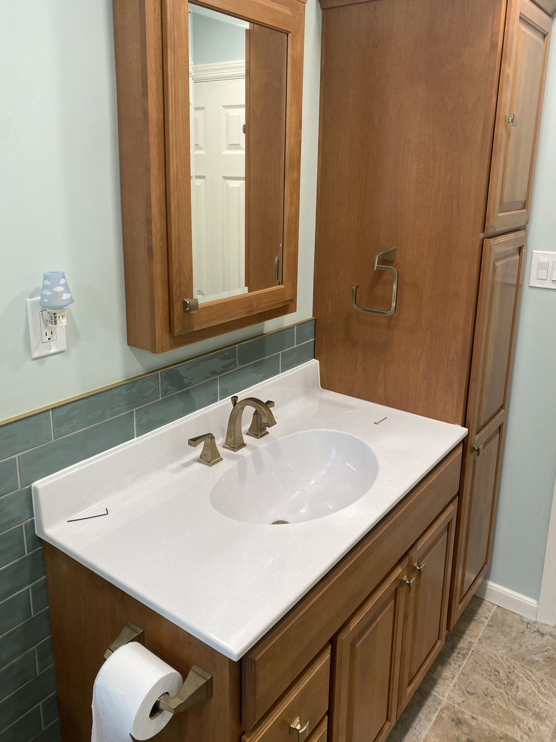 Bathroom with wooden cabinets, white countertop, oval sink, and a mirrored medicine cabinet.