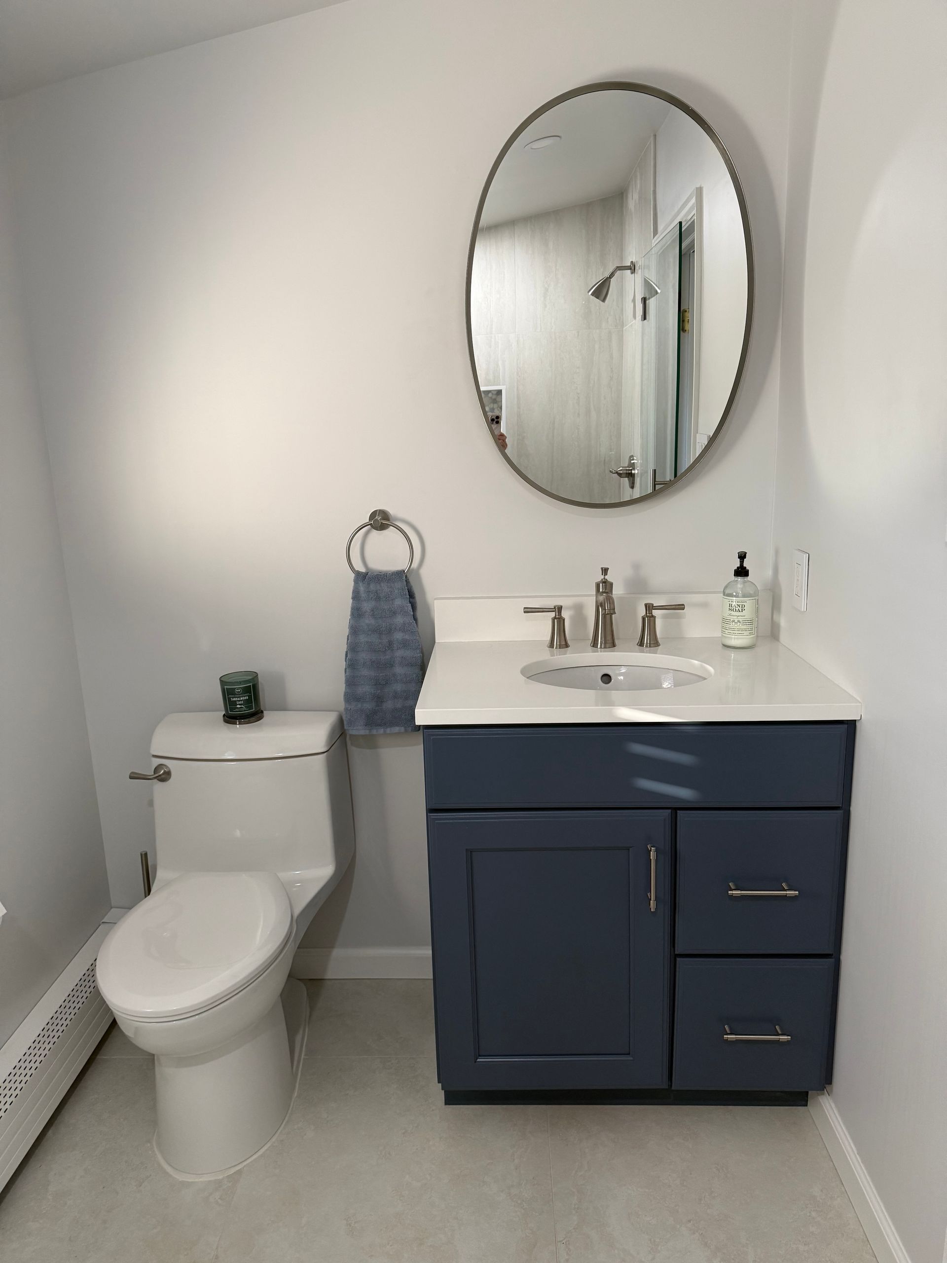 Small blue bathroom vanity with white countertop, round mirror, and toilet.