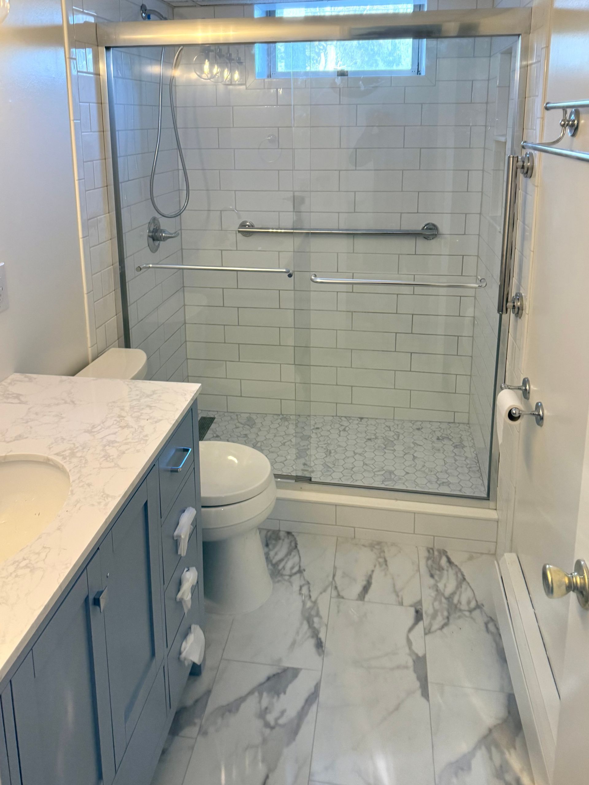 Bathroom with glass shower, white subway tile, marble floor, and blue vanity.