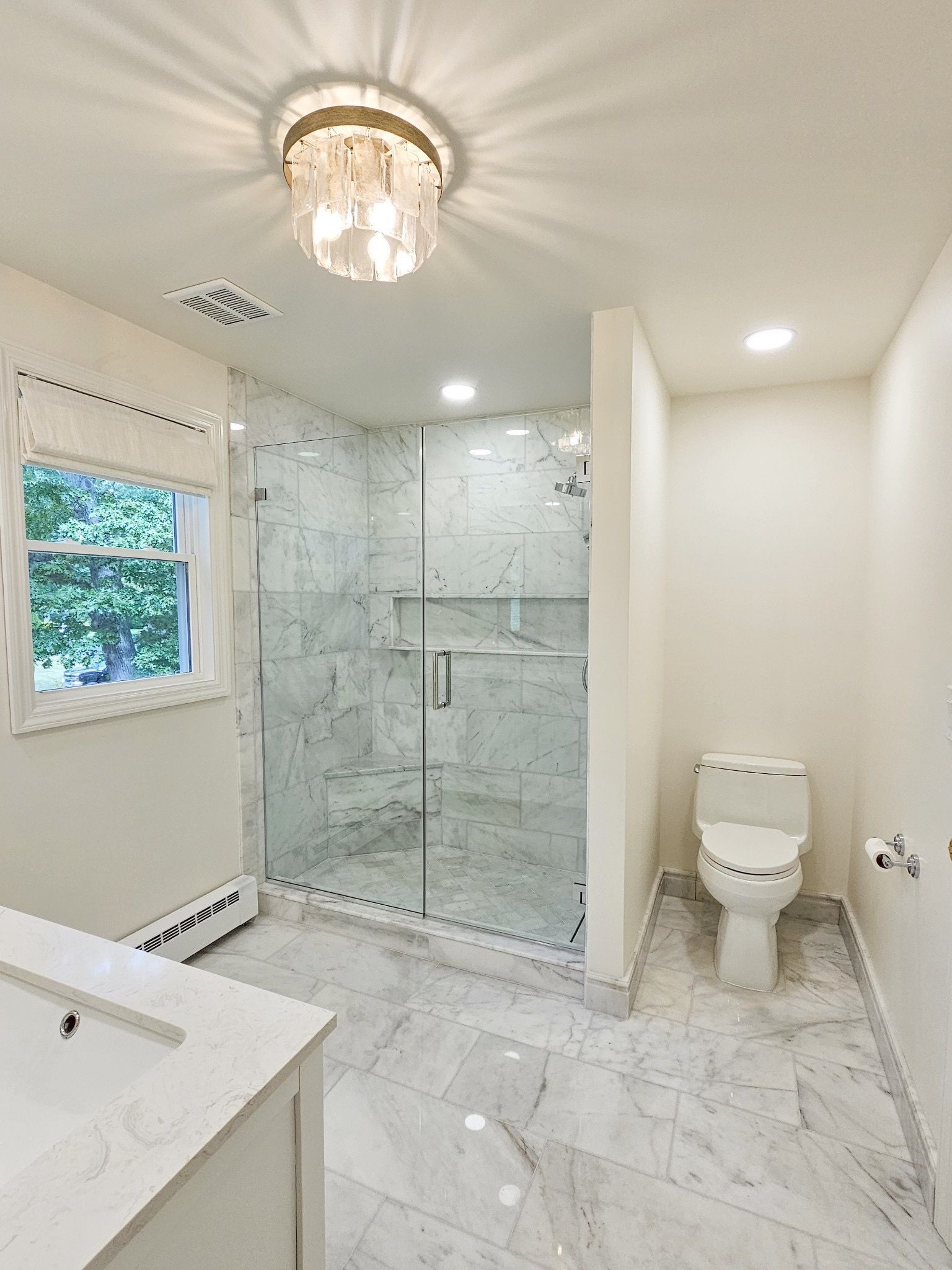 Modern bathroom with marble tile, glass shower, and toilet.
