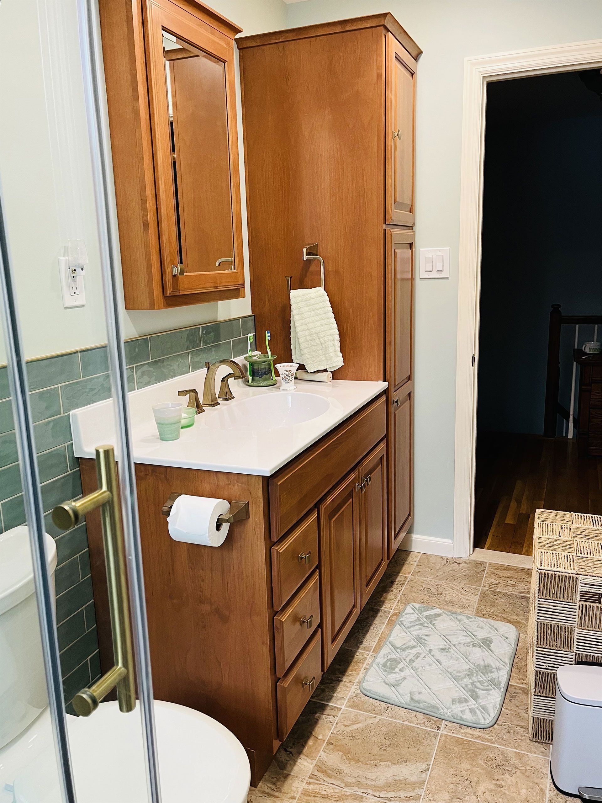 Bathroom with wood cabinets, white sink, green tile, and a patterned rug.