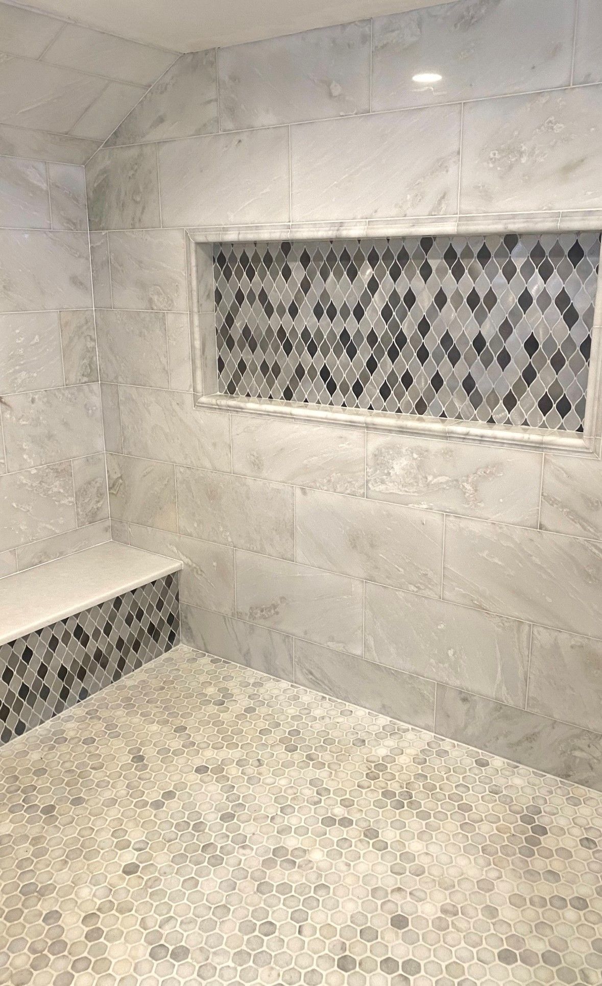 Shower with gray and patterned tile, built-in bench, and a tiled recessed shelf.