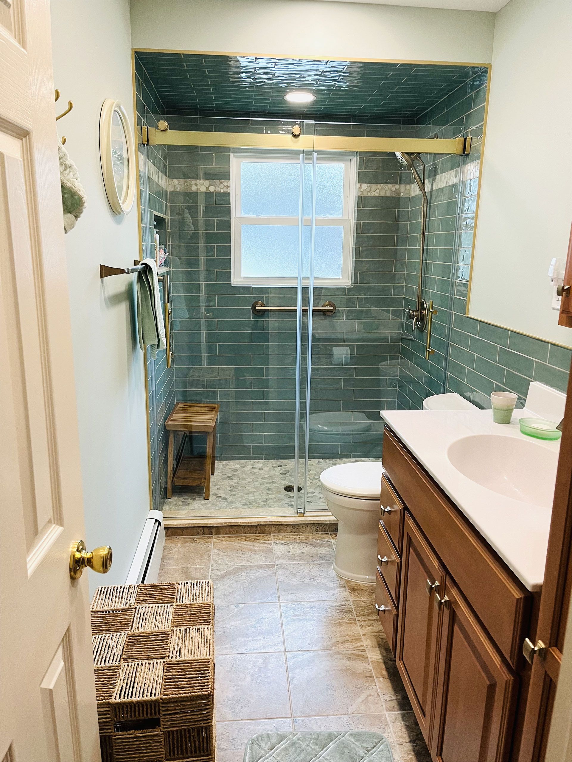 Bathroom with blue-tiled shower, wood vanity, and a small stool.