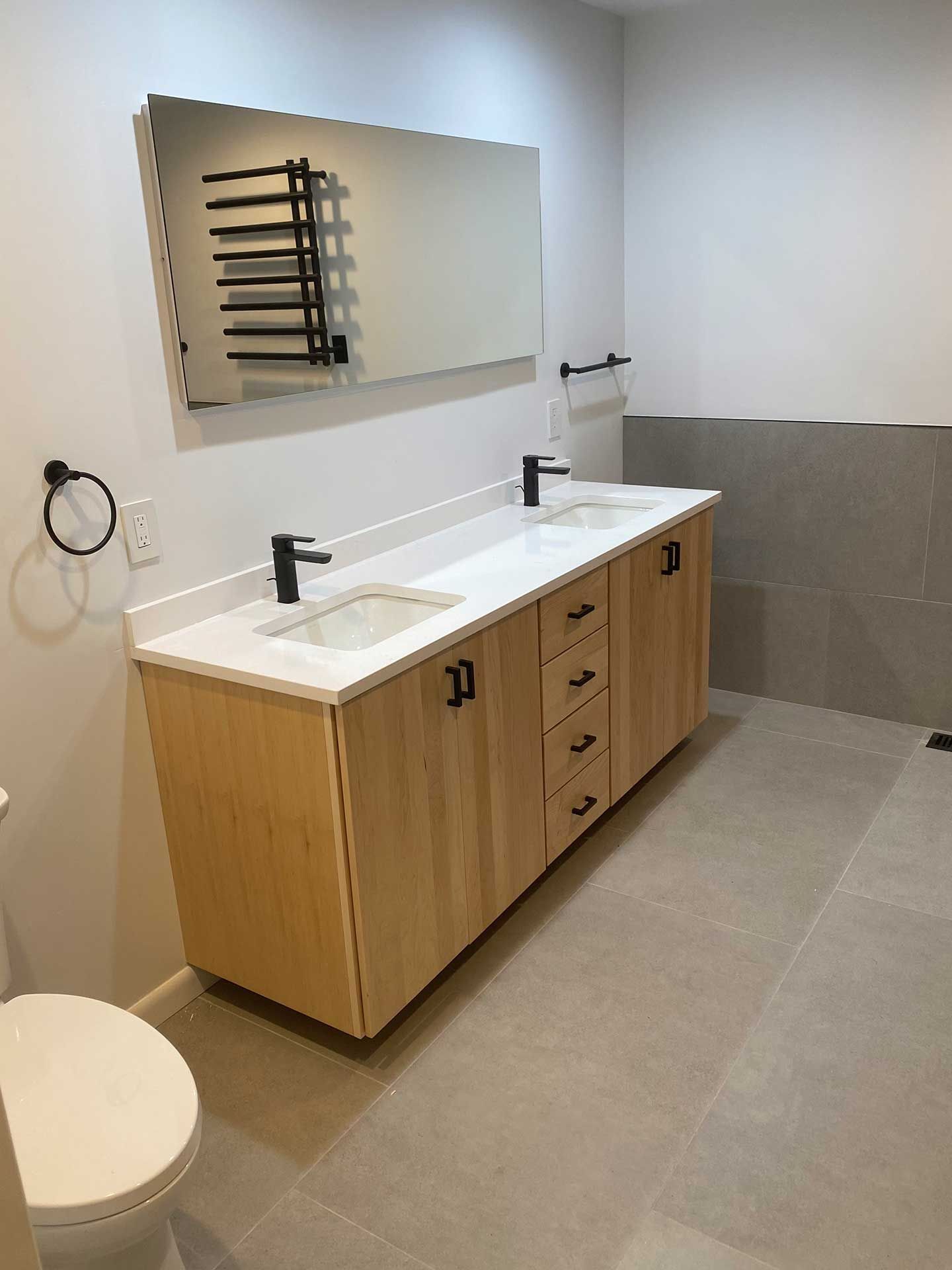 Bathroom with light wood double vanity, black fixtures, large mirror, and gray tile floor.