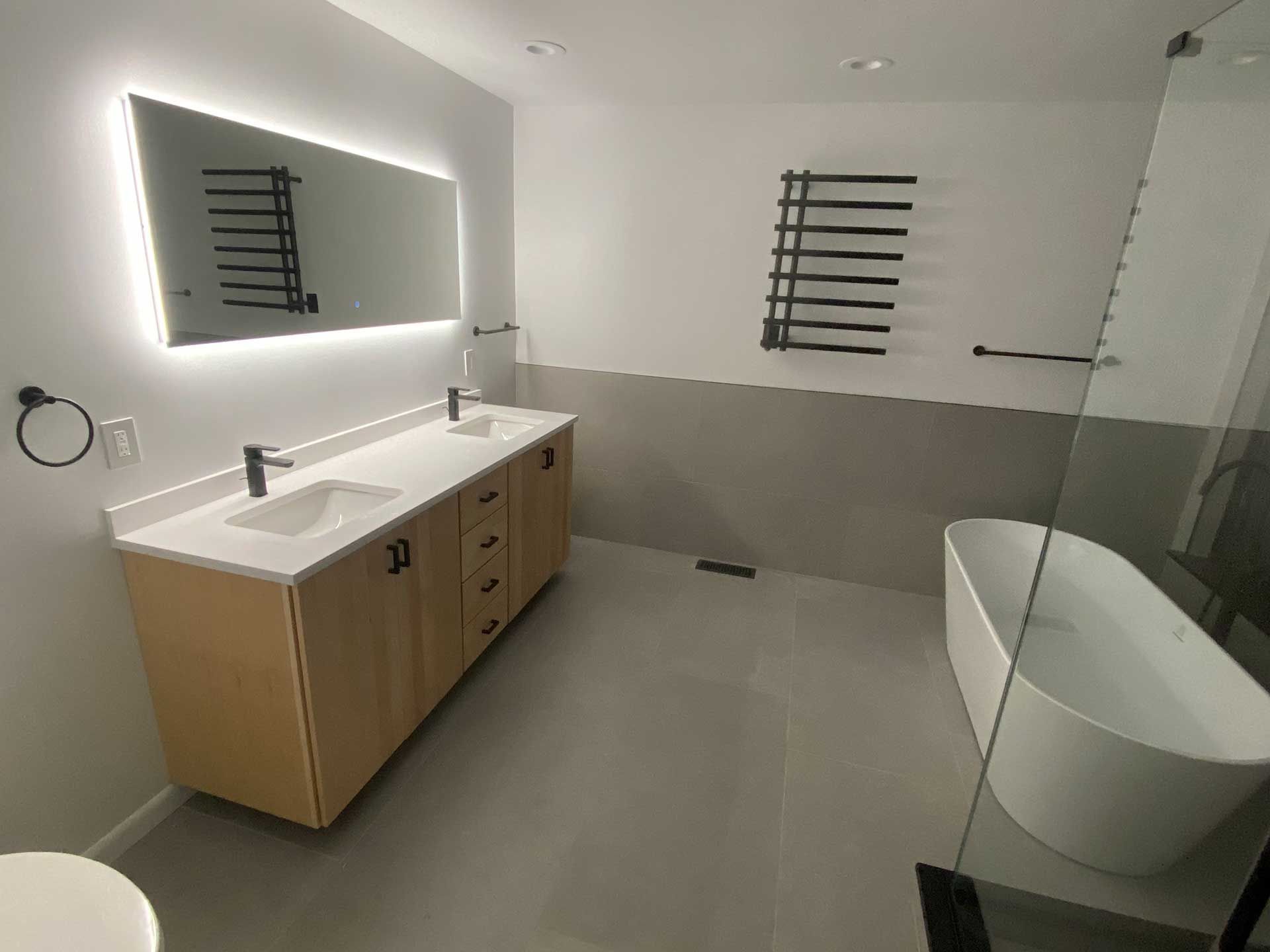 Modern bathroom with double vanity, bathtub, and heated towel rack. Neutral colors, minimalist design.