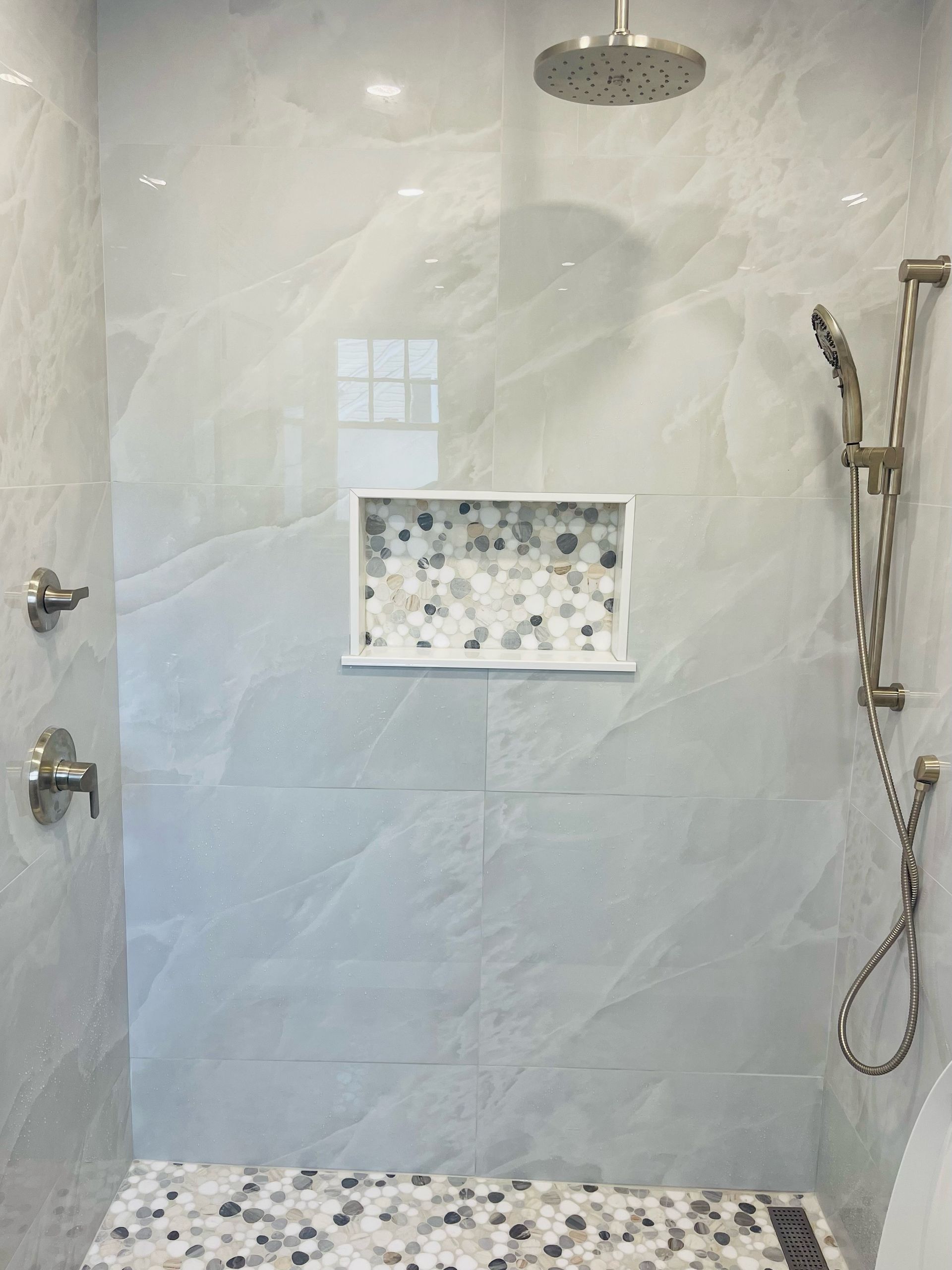 Shower with light gray tile walls, mosaic floor, and built-in shelf.