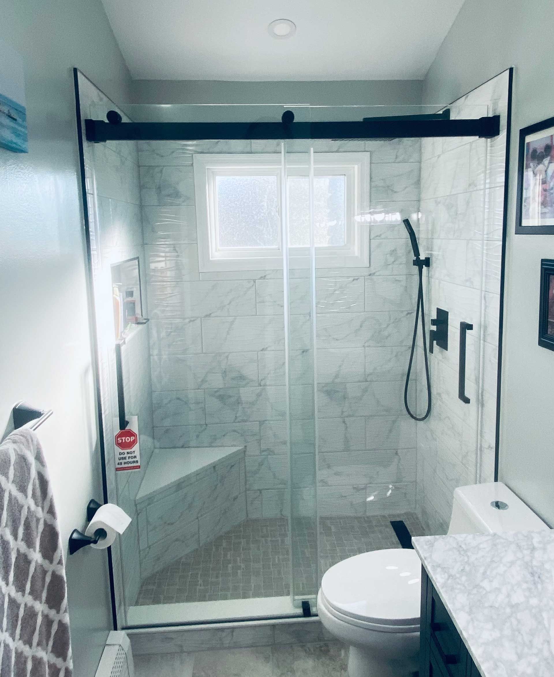 Modern bathroom with glass shower enclosure, black fixtures, and a toilet.