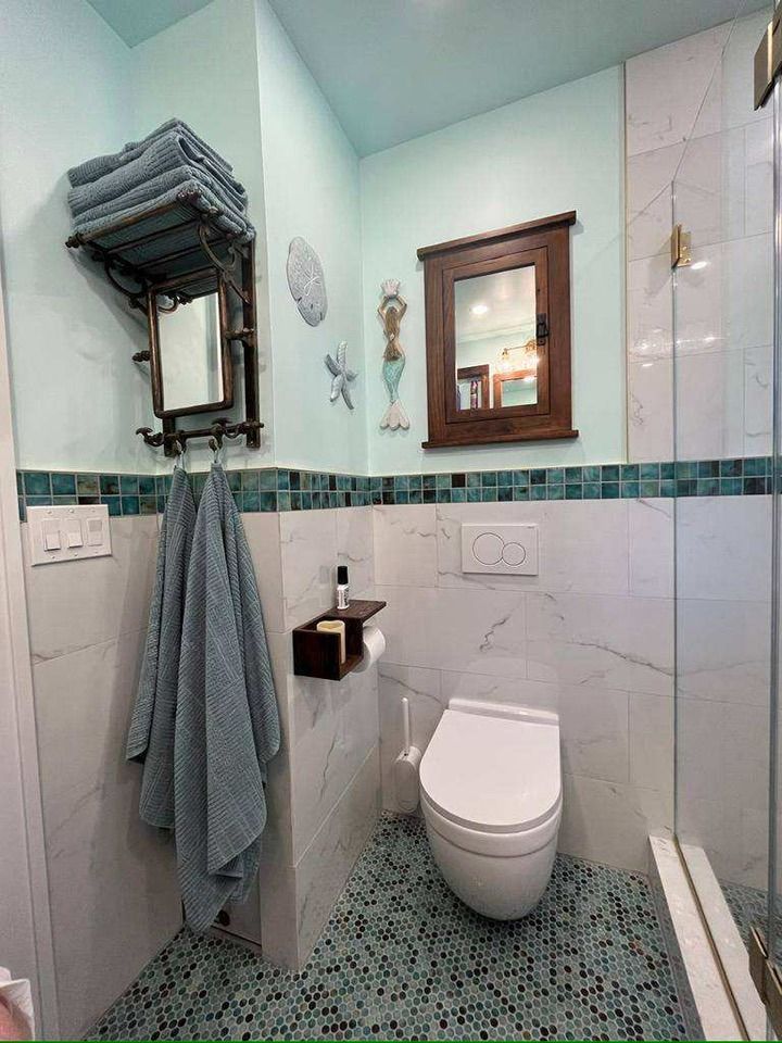 Bathroom with blue and white tile, a wall-mounted toilet, and a shelf with towels.