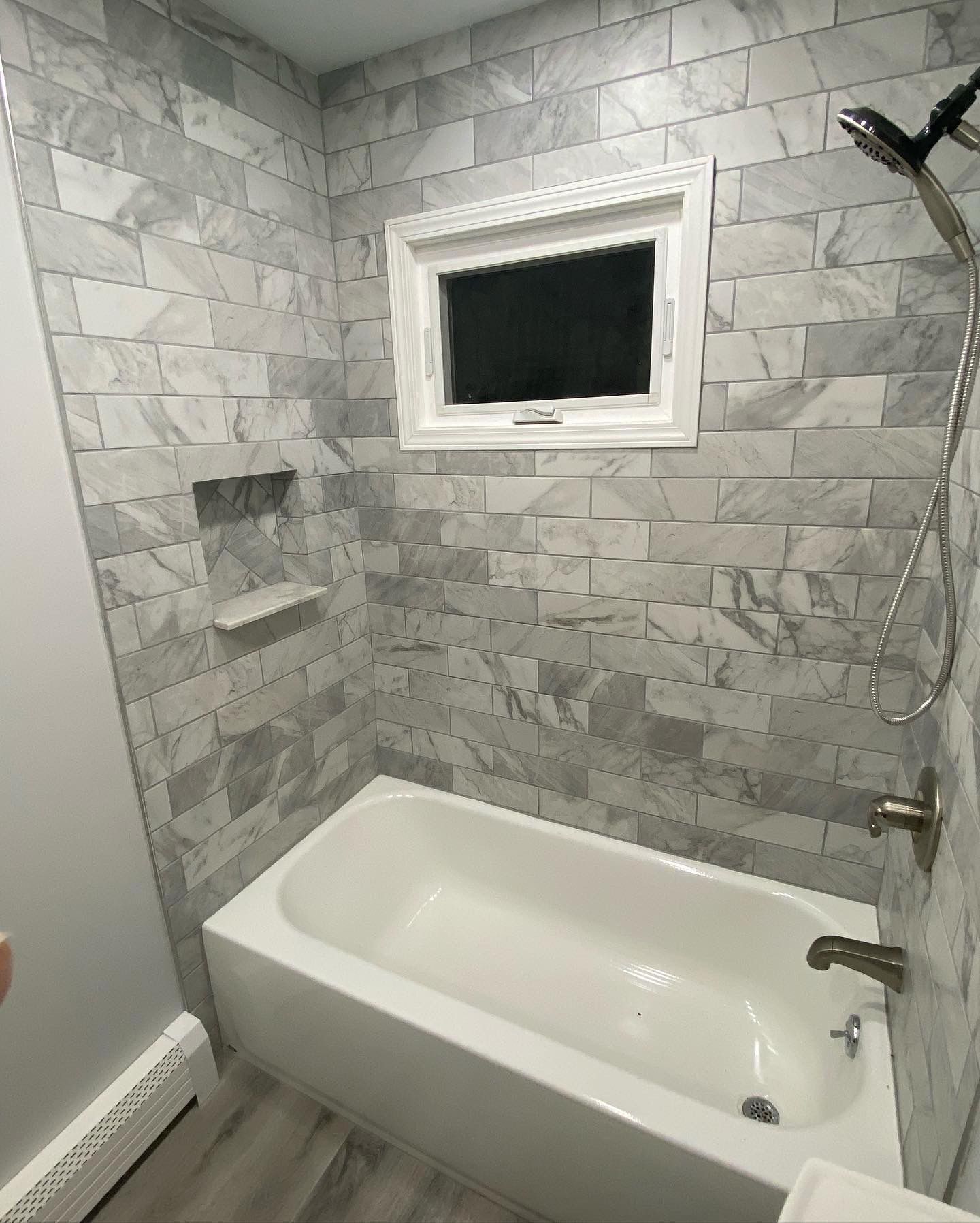 Bathroom with white bathtub, gray tiled walls, and small window.