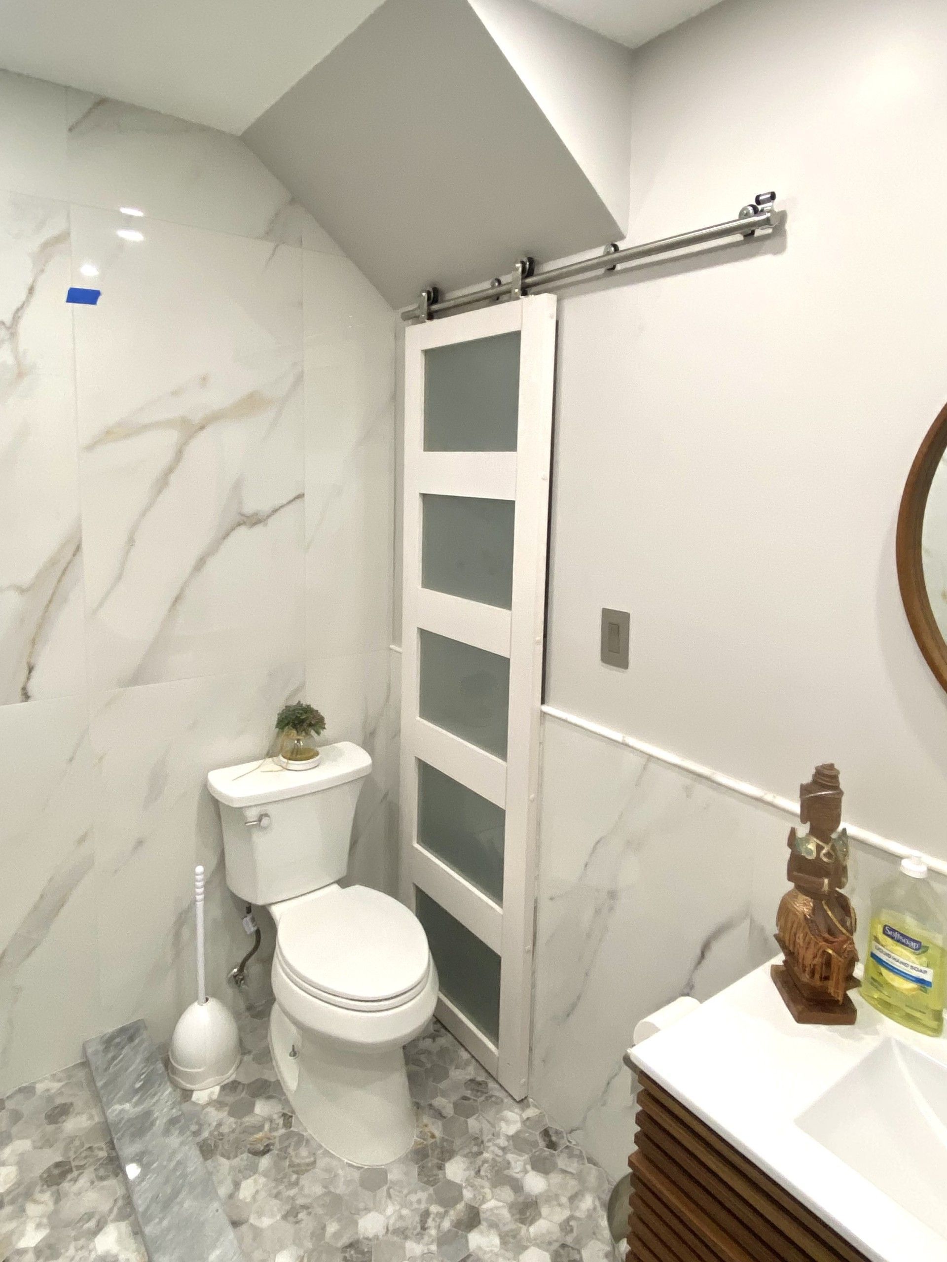 Bathroom with white marble tile, toilet, frosted sliding door, and wood vanity.