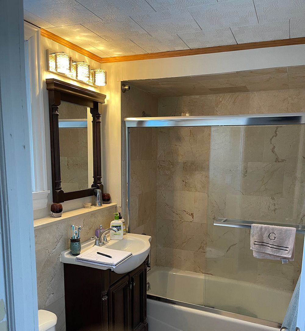 Bathroom with a dark wood vanity, mirror, and a tub/shower combination. Beige tile and trim.
