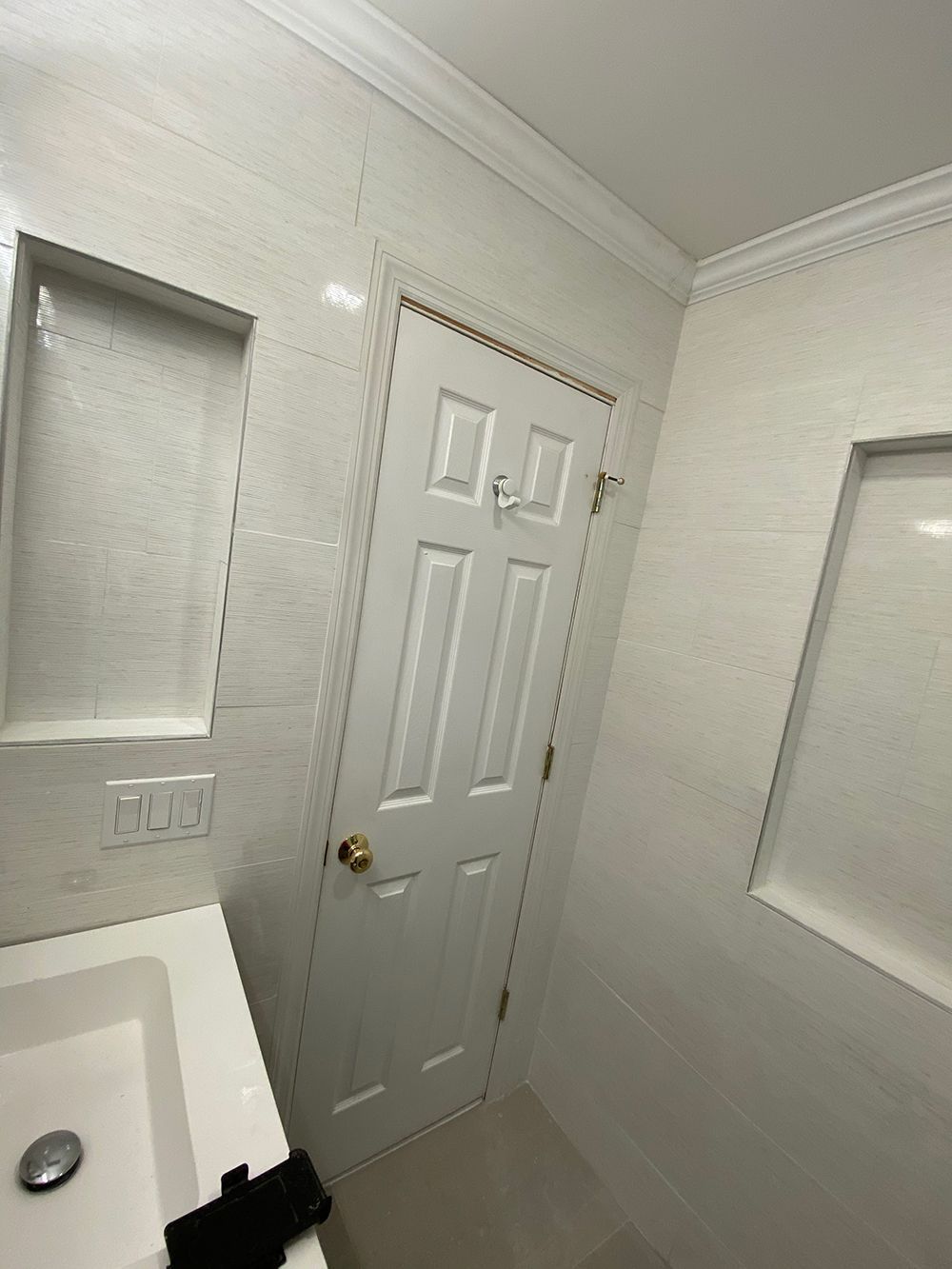 Bathroom with white tile walls, a white door, and built-in shelving.