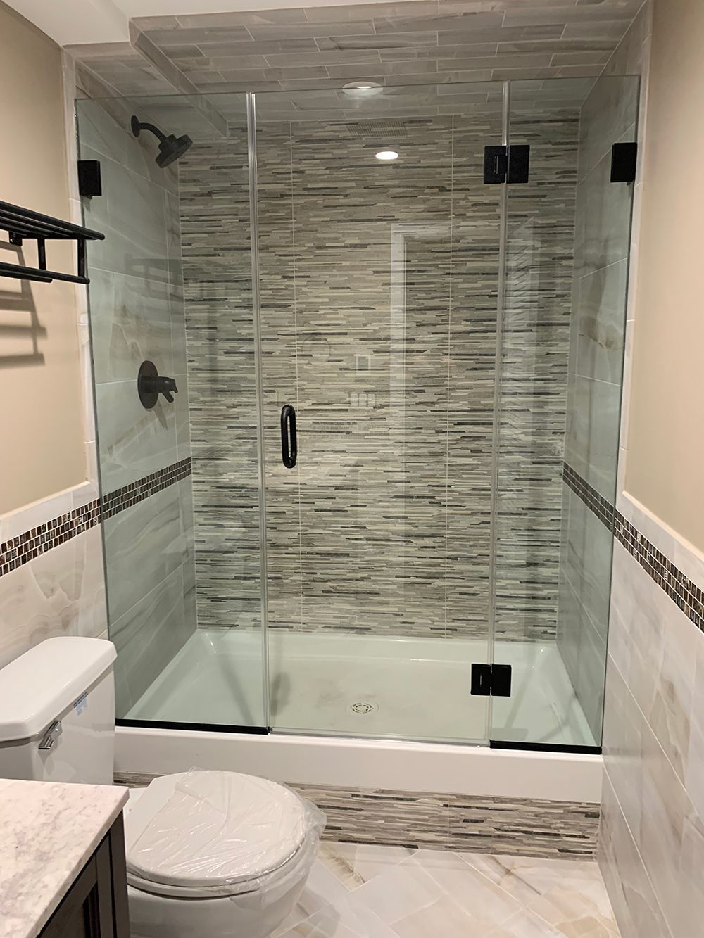 Shower enclosure with glass doors, black hardware, and tiled walls and floor.