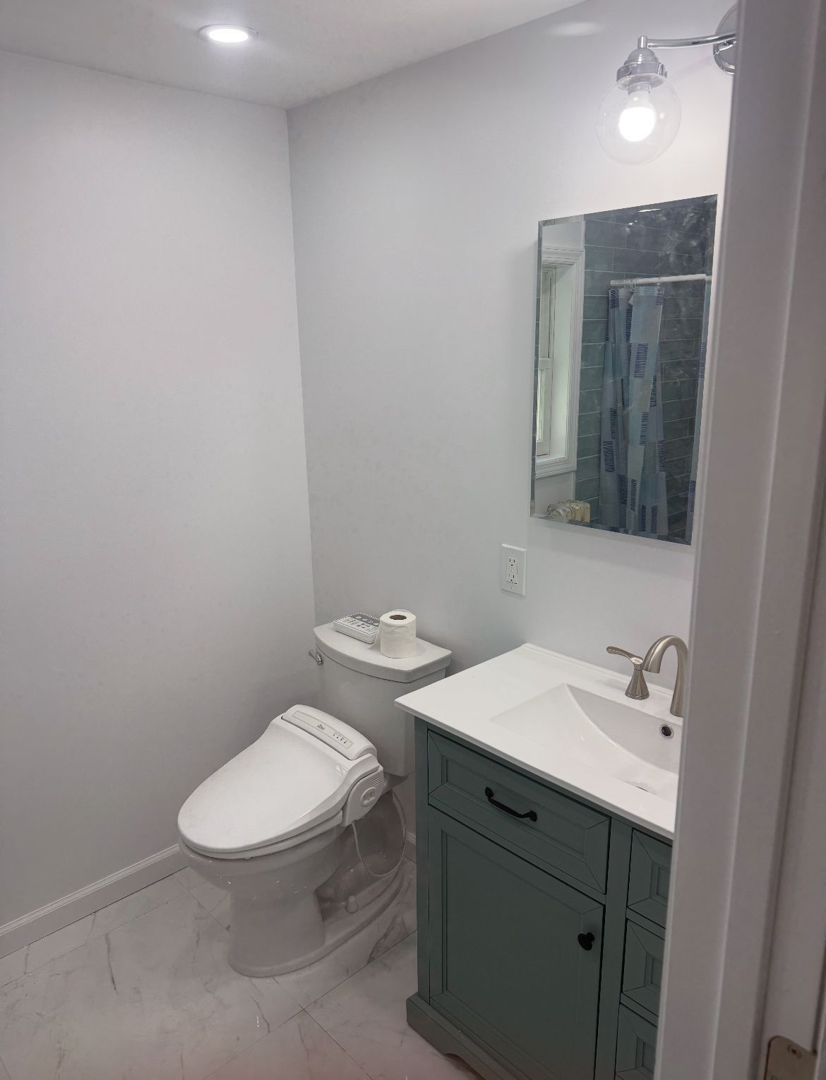 Bathroom with white walls, a blue vanity, a toilet with a bidet seat, and a mirror with a light fixture.