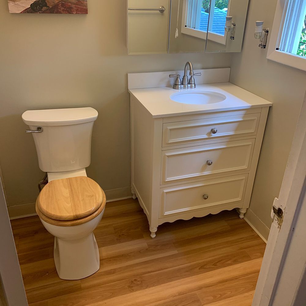 Small white bathroom with a toilet and sink vanity on wood-look flooring.