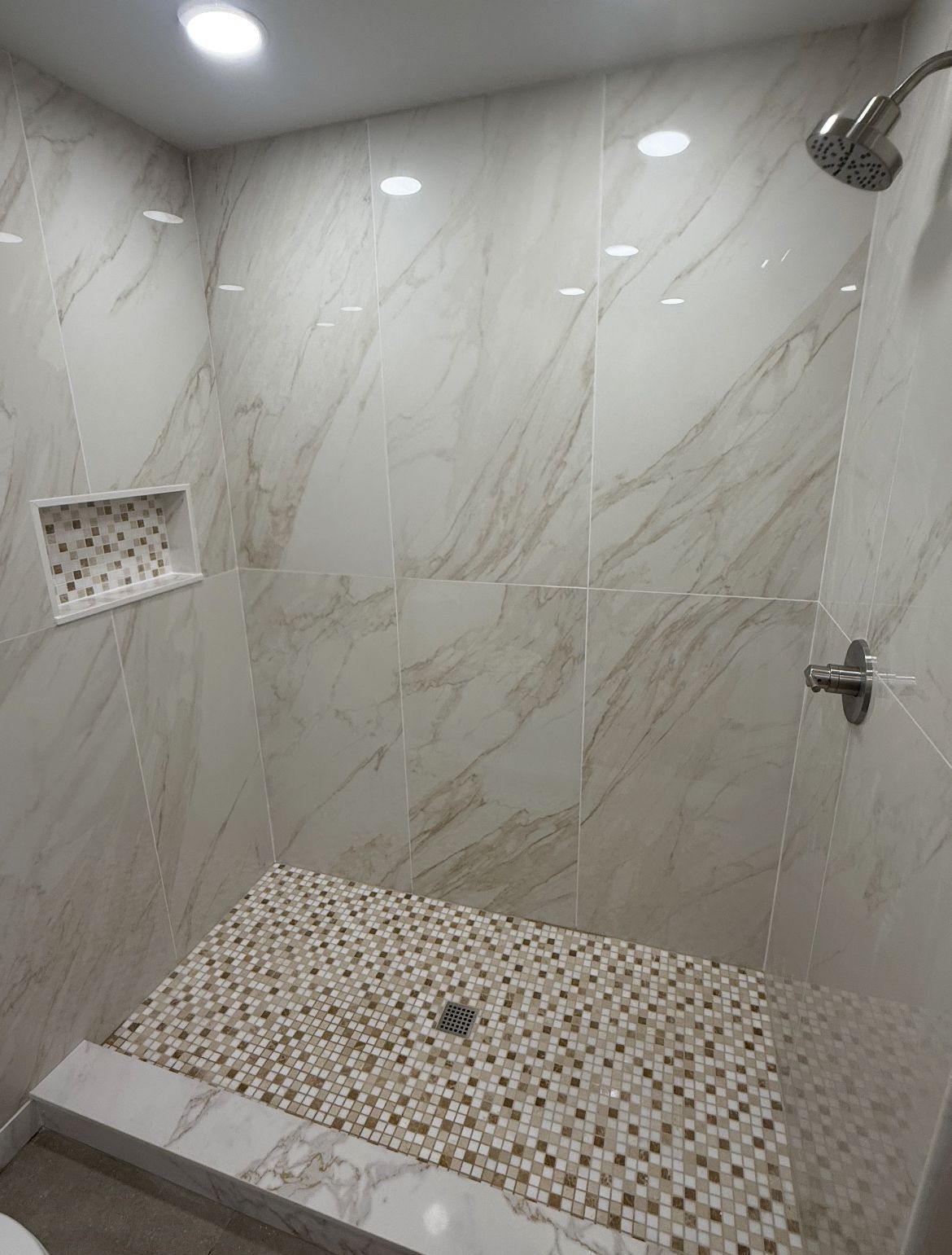 Shower with marble-look tile walls, pebble floor, and recessed shelf.