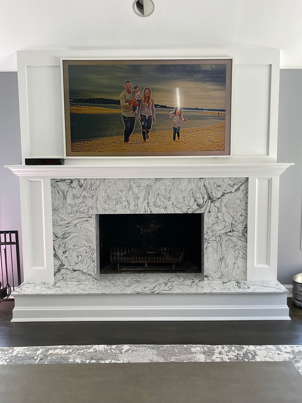 Fireplace with family photo above, white trim, speckled grey stone, gray walls, and wooden floor.