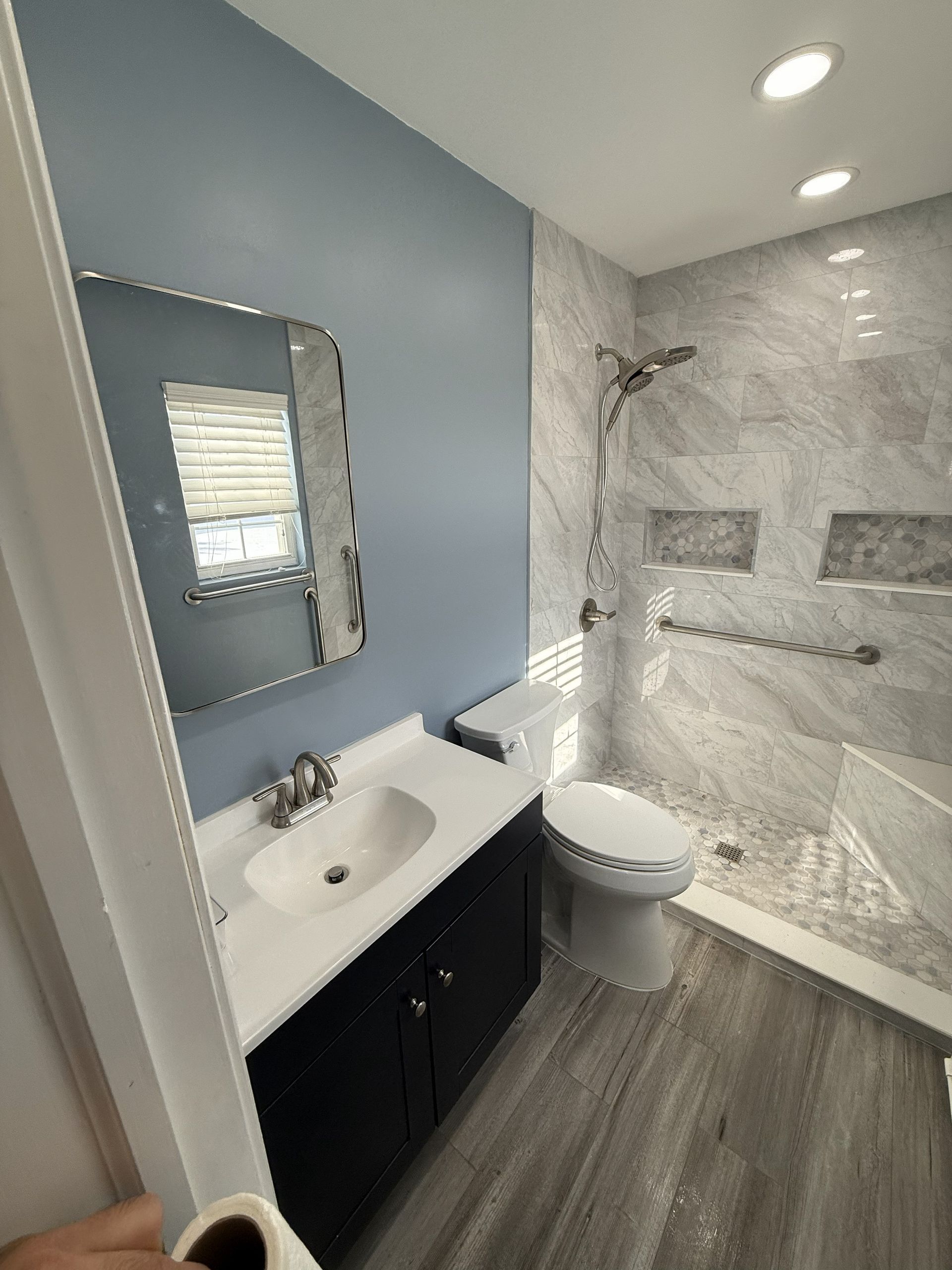 Bathroom with blue walls, black vanity, marble-tiled shower, and accessible grab bars.