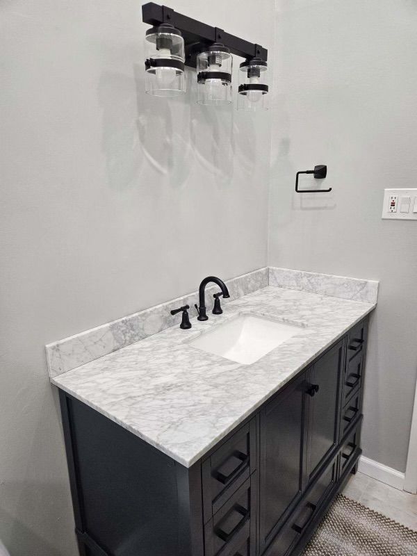 Bathroom vanity with marble countertop, dark gray cabinet, black fixtures, and three-light sconce.
