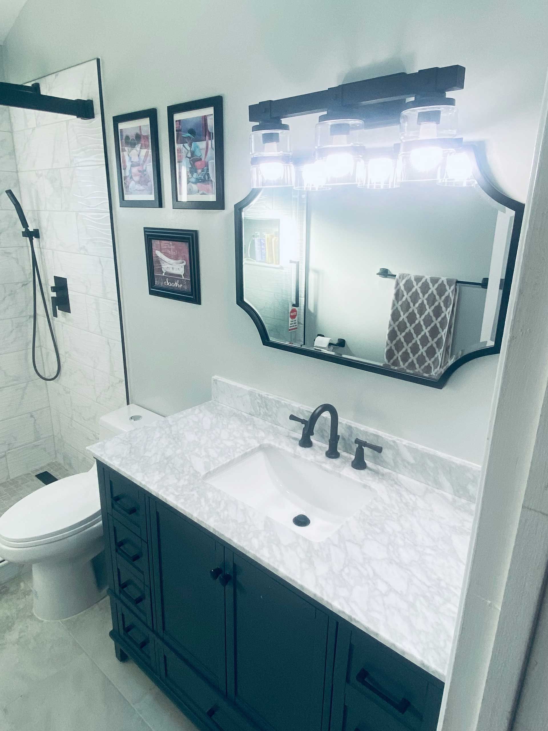 Bathroom with dark vanity, black framed mirror, shower, and framed art.
