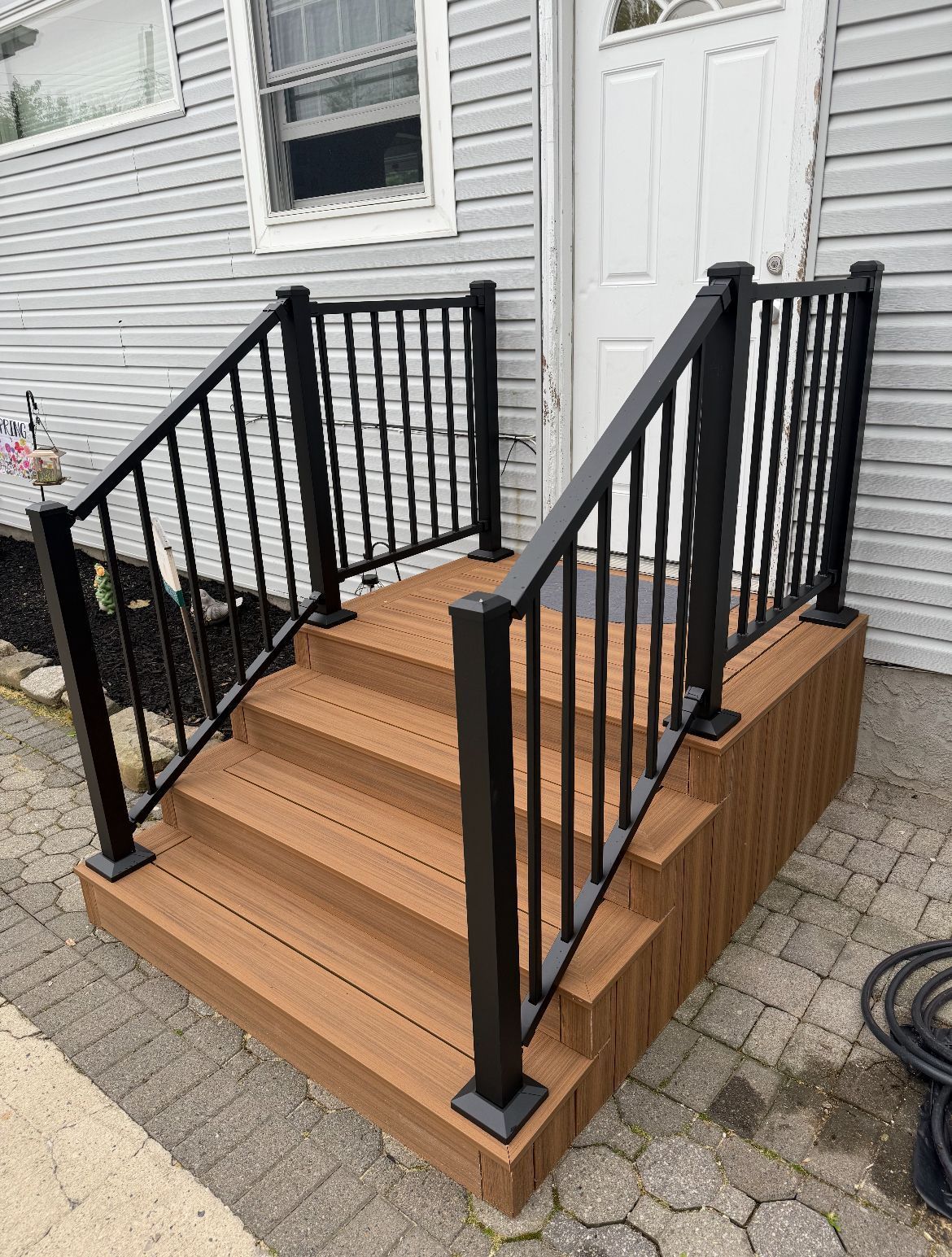 Brown composite stairs with black railings leading to a white door.