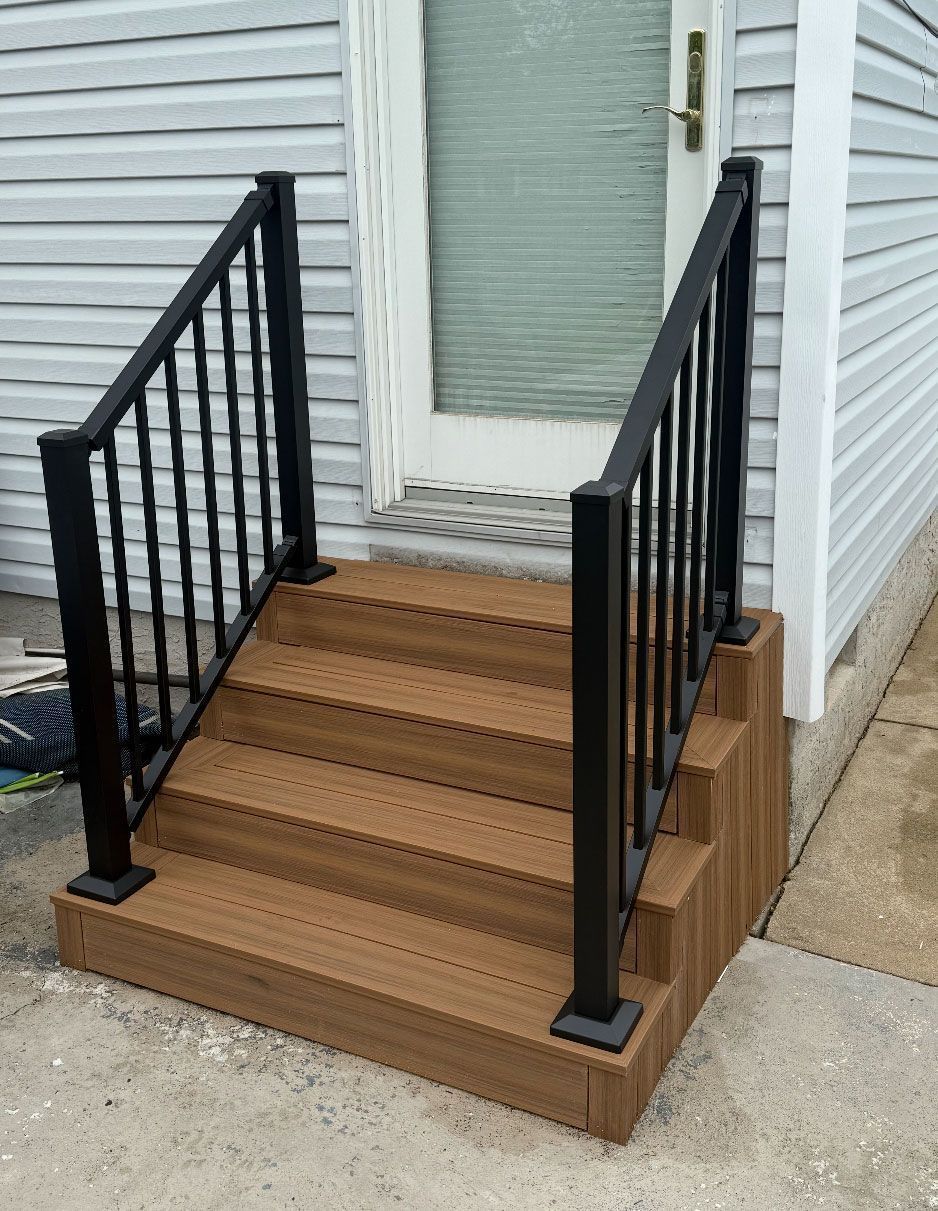 Brown composite steps with black metal railing leading to a white door.